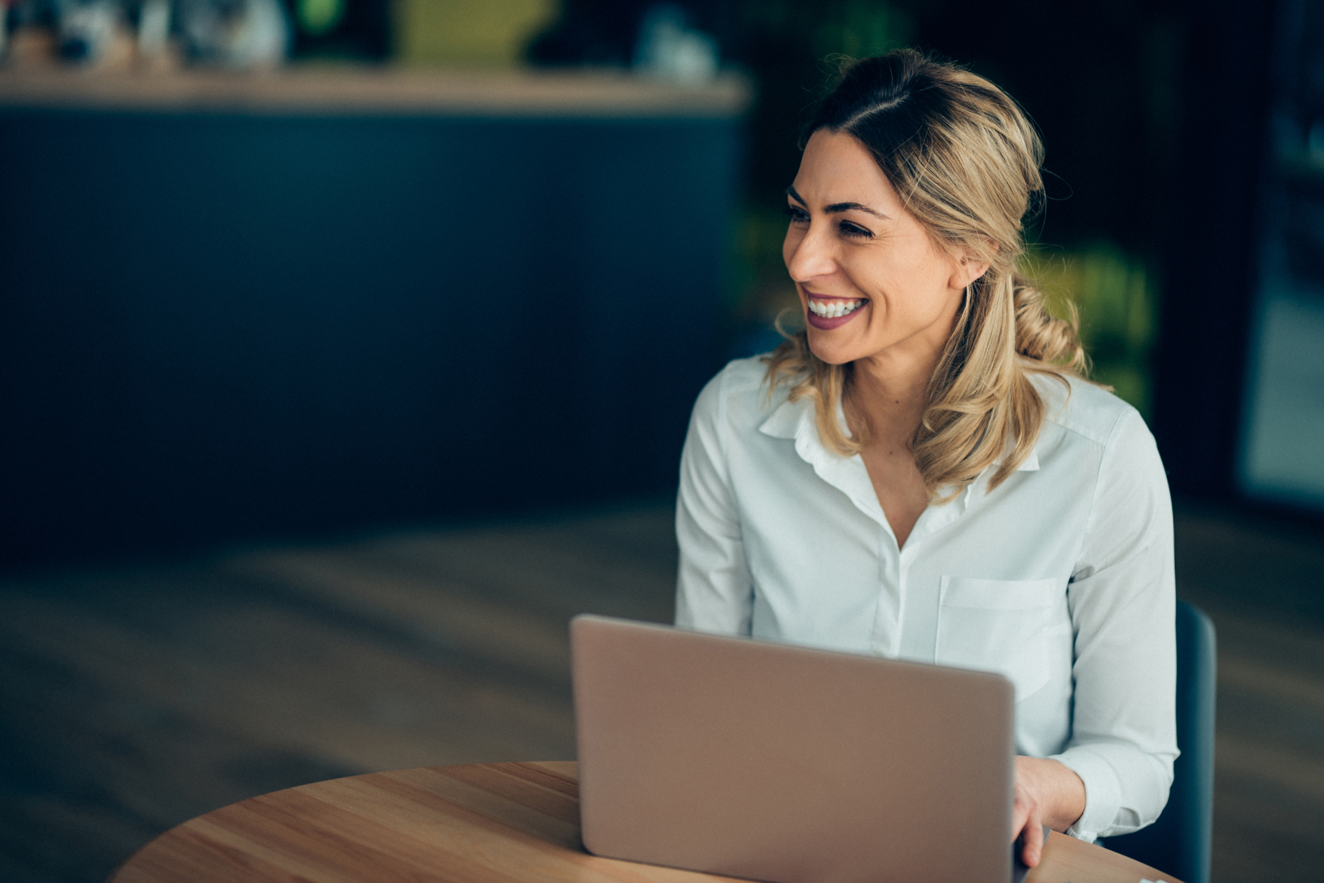 Lady smiling as she sits at a table working on her laptop