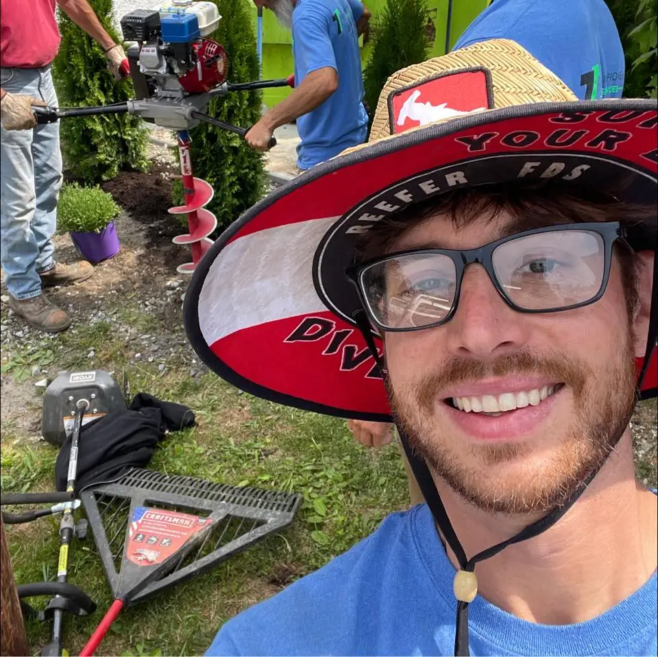 James Thompson owner of Thompson Improvements Pro Services is wearing a large brimmed hat and smiling with his team landscaping in the background