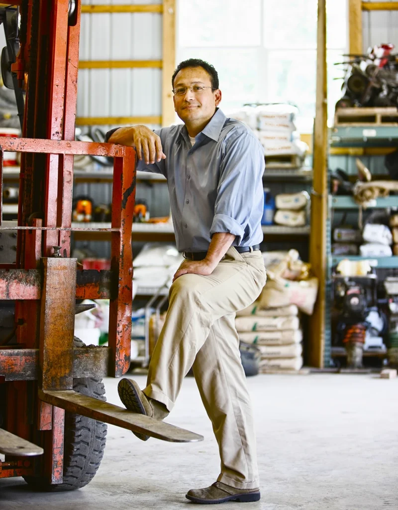 Business owner standing beside a forklift in a warehouse, representing small business leadership and growth strategy.